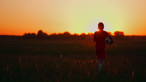Der-Junge-Steht-Bei-Sonnenuntergang-Mit-Einem-Fußball-Auf-Dem-Feld-Im-Gras.-Er-Träumt-Von-Einer-Fußballkarriere.-Das-Konzept-Des-Erfolgs-Im-Sport.